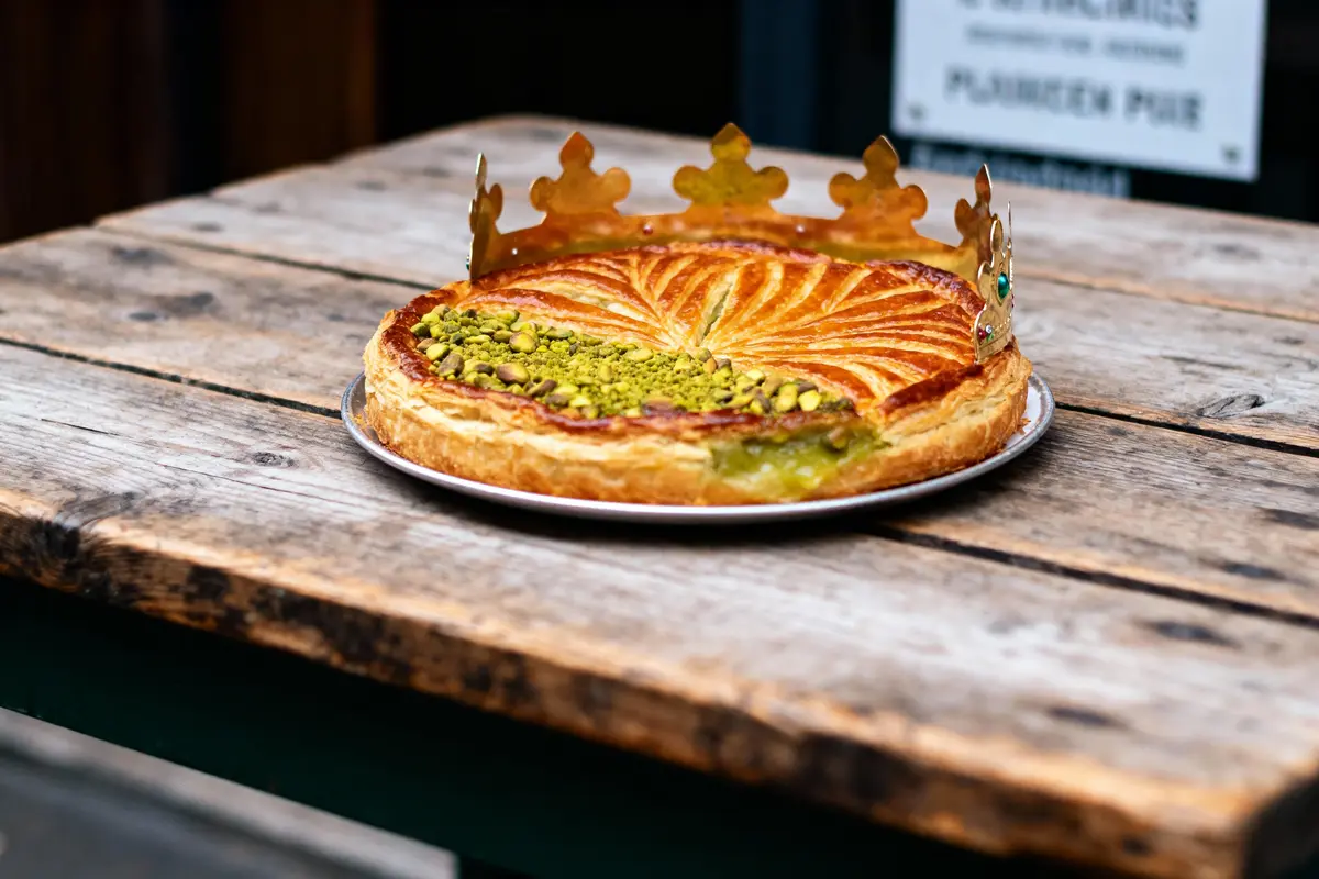 Galette des rois sur table en bois, couronne dorée, garniture pistache, décor feuilleté doré.