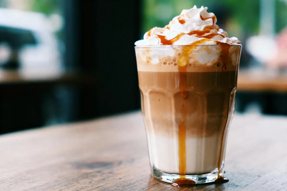Verre de café latte avec crème fouettée et caramel sur table en bois.