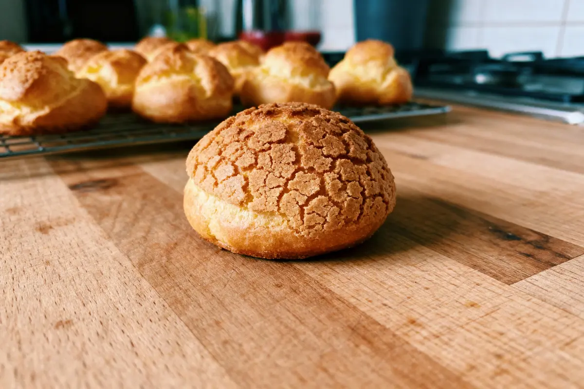Pâtisseries dorées sur planche de bois, chou craquelin en gros plan avec d'autres en arrière-plan.