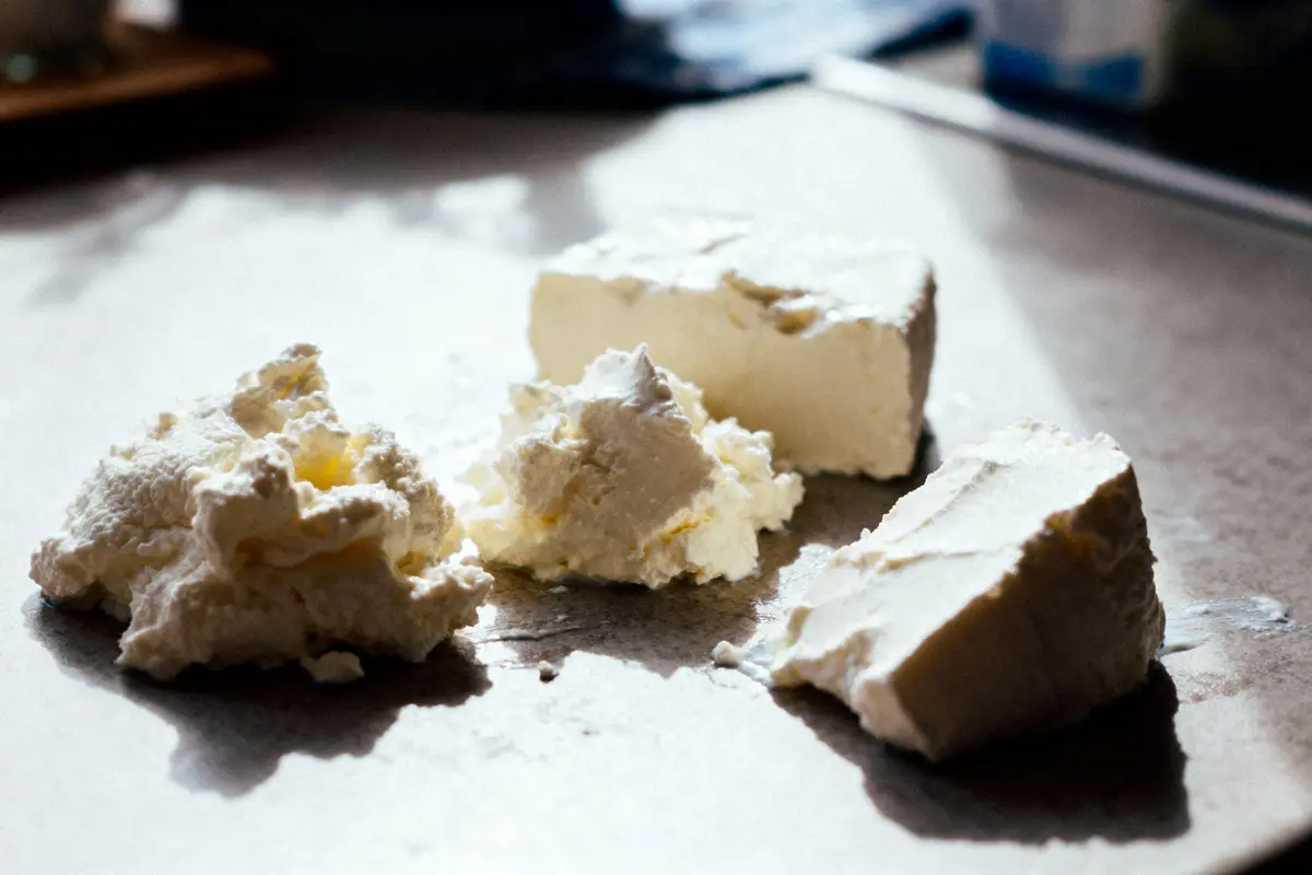 Quatre morceaux de fromage blanc sur une surface, éclairés par une lumière naturelle douce.