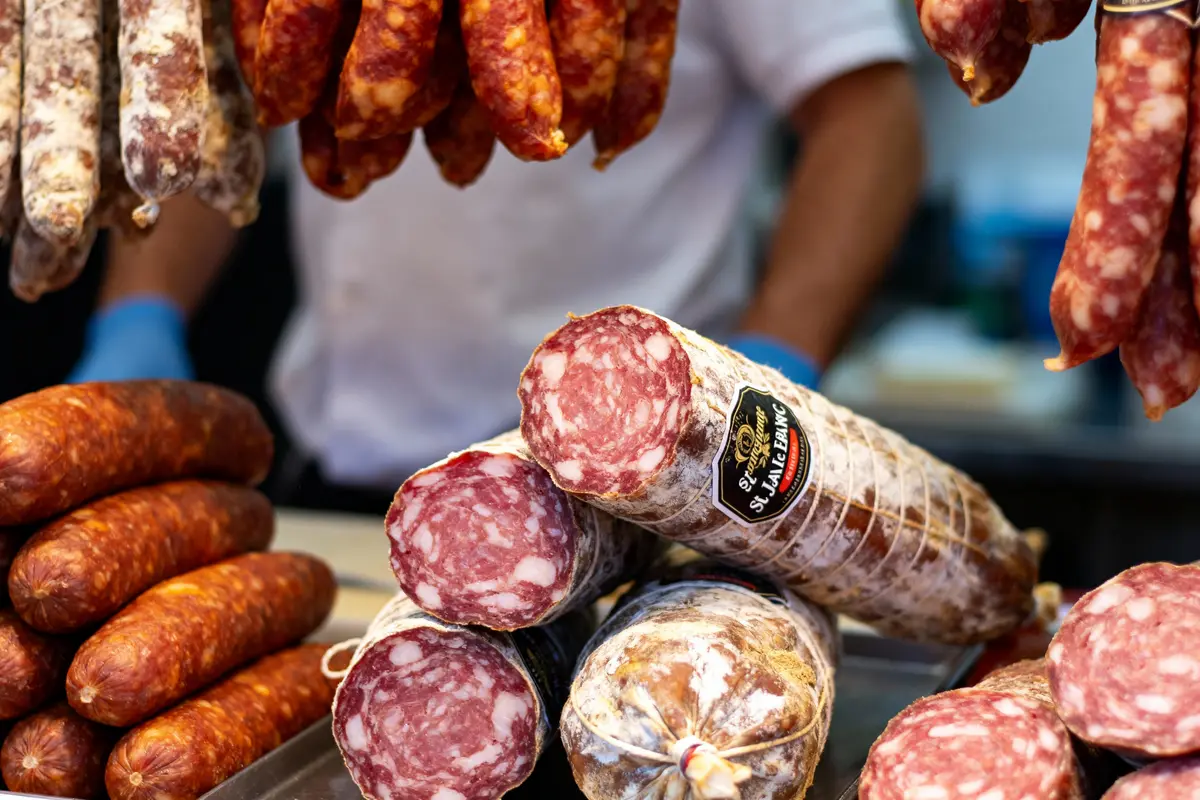 Assortiment de saucissons à la charcuterie avec étiquette. Boucher flou en arrière-plan, portant des gants bleus.