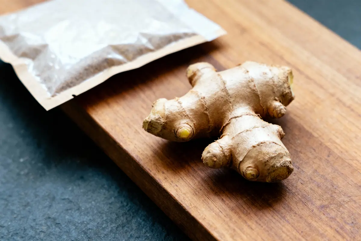 Racine de gingembre et sachet de poudre sur planche en bois, vue rapprochée.