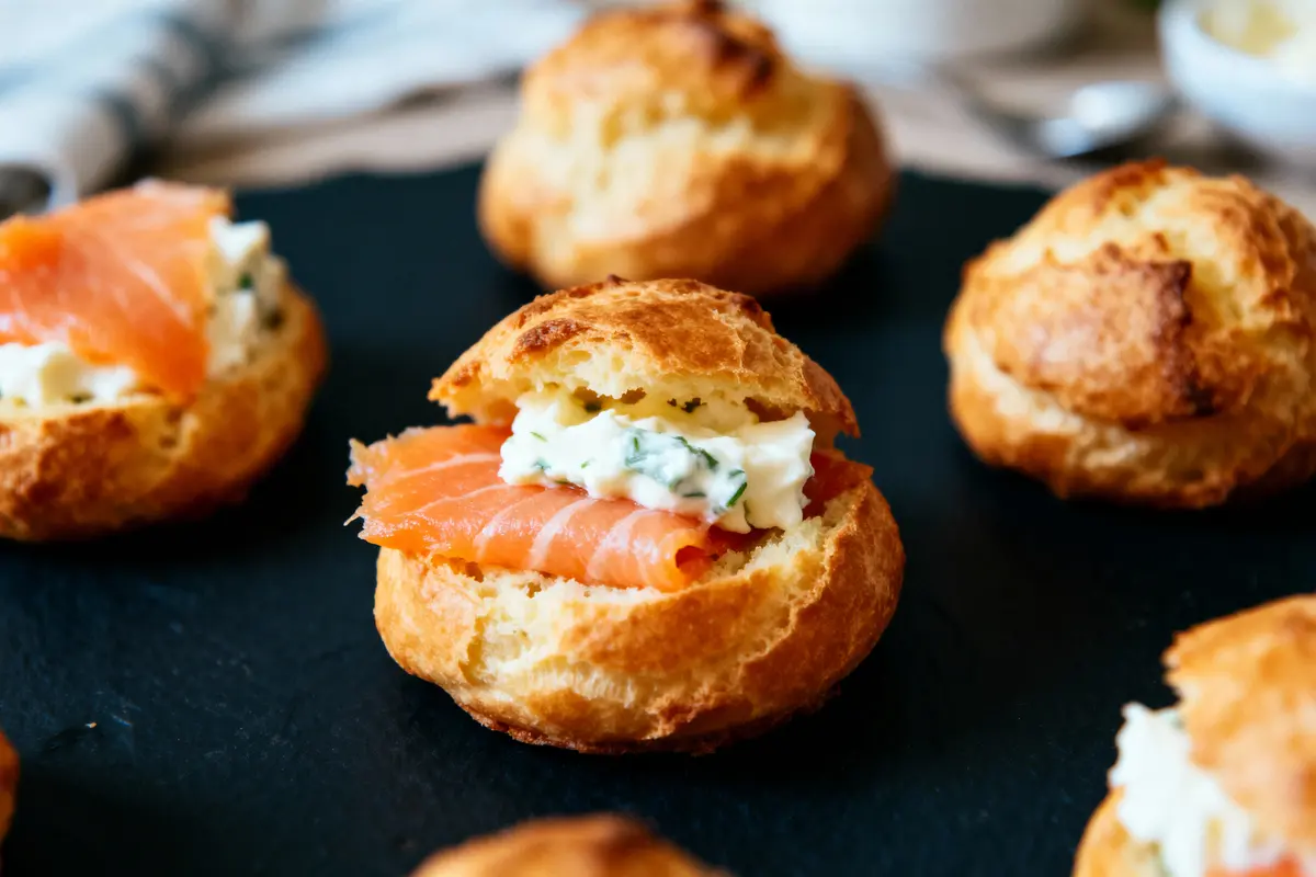 Choux garnis de saumon fumé et crème, sur une surface noire.