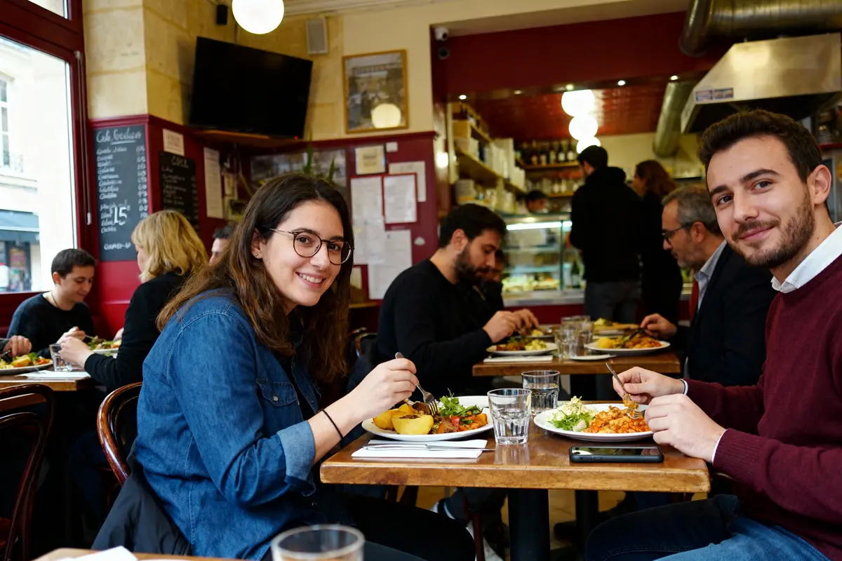 Des personnes dînent joyeusement dans un restaurant animé, savourant des plats colorés et variés sur des tables en bois.