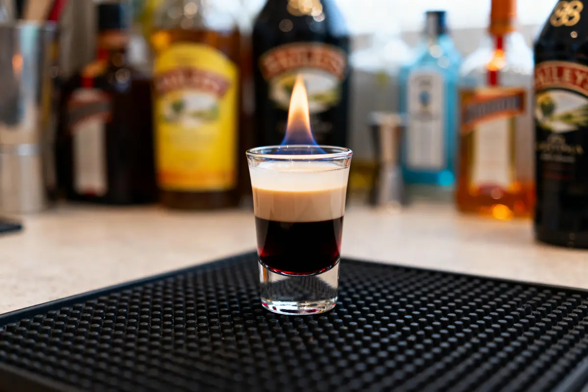 Verre à shot enflammé avec cocktails en arrière-plan sur un bar.