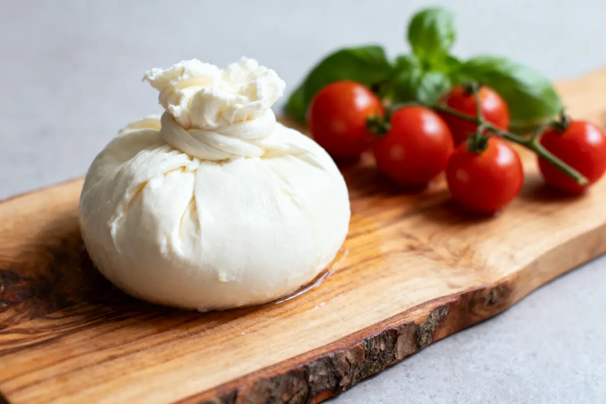 Burrata sur planche en bois avec tomates cerises et feuilles de basilic en arrière-plan.
