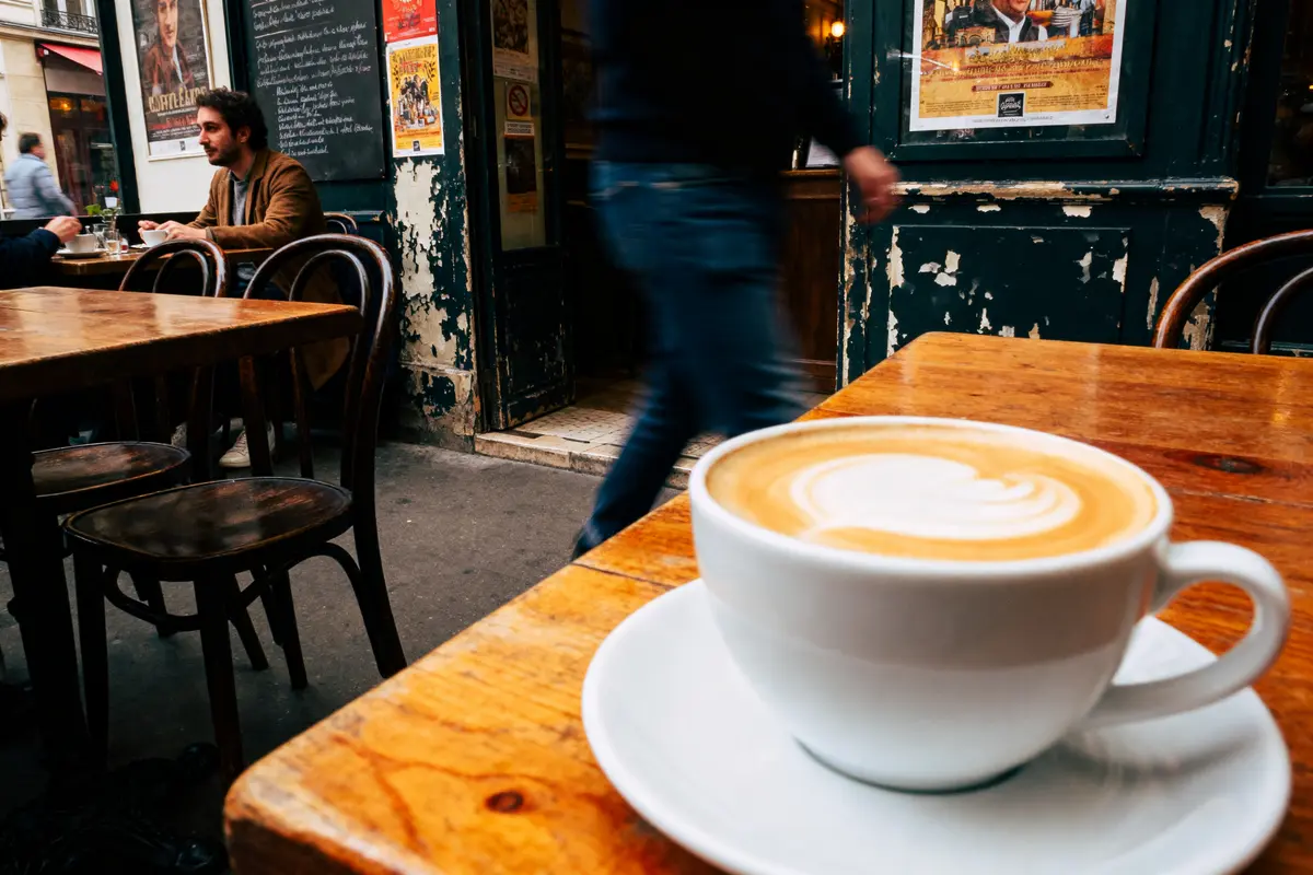 Tasse de café sur table de café parisien, homme en arrière-plan, atmosphère animée et urbaine.