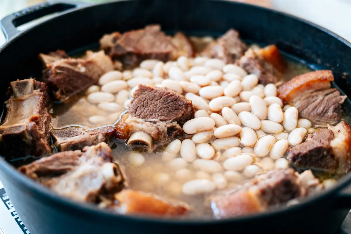 Plat en cocotte avec haricots blancs et morceaux de viande mijotée dans un bouillon savoureux.
