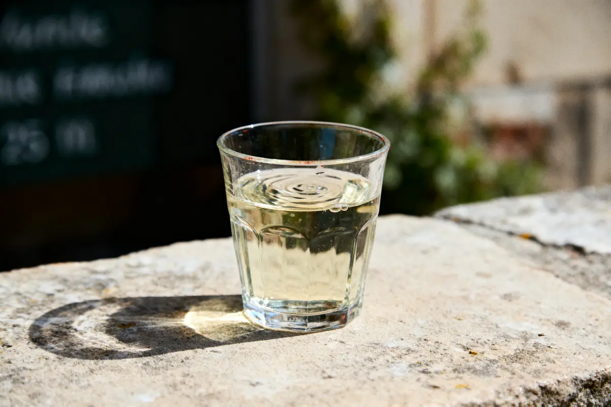 Verre de vin blanc sur une surface en pierre, lumière du soleil et arrière-plan flou.
